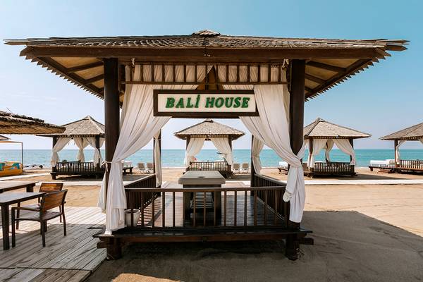 Bali House Strandpavillon mit weißen Vorhängen und Blick auf das Meer.