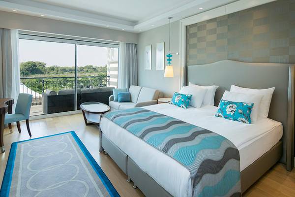 Hotelzimmer im Titanic Deluxe Golf Belek mit großem Bett, Wohnzimmerbereich und Balkon.