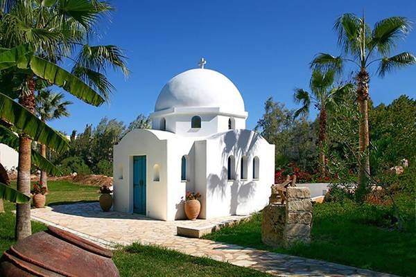 Weiße kleine Kirche im Azia Resort & Spa mit blauer Tür und Kreuz auf dem Dach