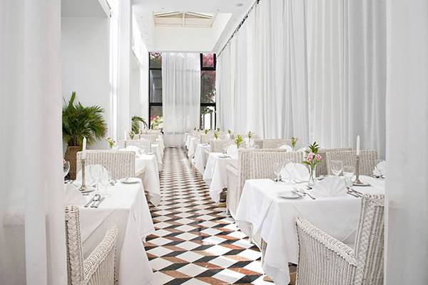 Innenansicht des Restaurants im Azia Resort & Spa mit weißen Tischen und Stühlen, gemustertem Boden und weißen Vorhängen.