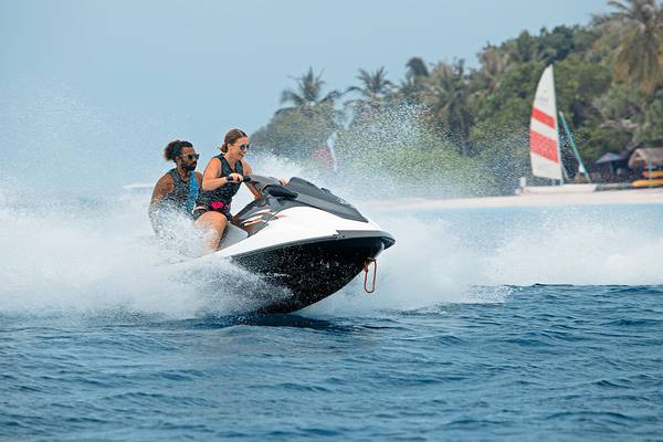 Zwei Personen auf einem Jetski im Wasser, eine Frau vorne und ein Mann hinten.