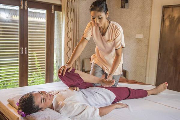 Massagebehandlung im Bandos Maldives Hotel, eine Frau liegt auf einem Bett, während eine Masseurin ihr Bein massiert.