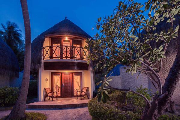 Abends beleuchtetes Bandos Maldives Hotel Bungalow mit Veranda und zwei Stühlen vor der Tür.