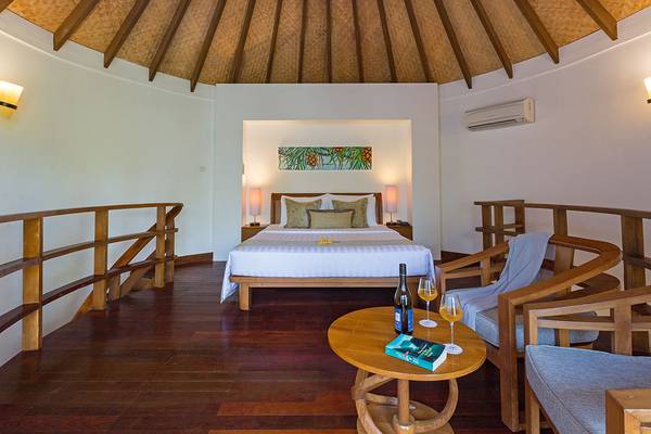 Schlafzimmer im Bandos Maldives Hotel mit einem Bett, einem Tisch mit Weinflasche und Gläsern und einem hölzernen Deckendach.