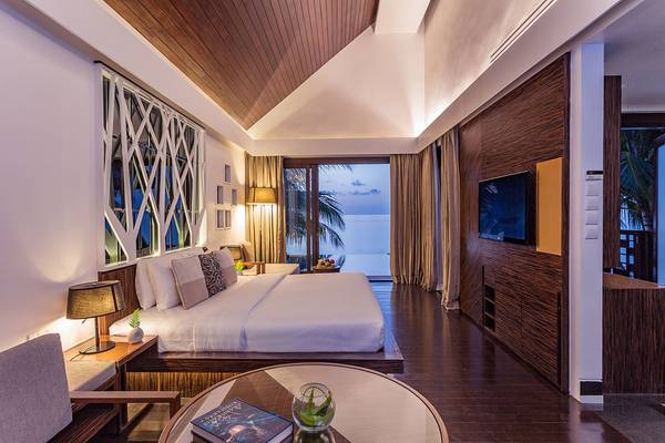 Schlafzimmer im Bandos Maldives Hotel mit Meerblick, großem Bett, Fernseher, Tisch mit Buch und Lampe.