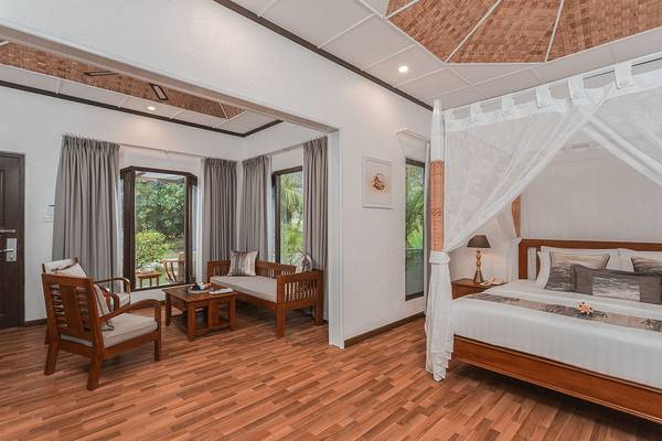 Innenansicht des Schlafzimmers im Bandos Maldives Hotel mit Bett, Möbeln und Aussicht.