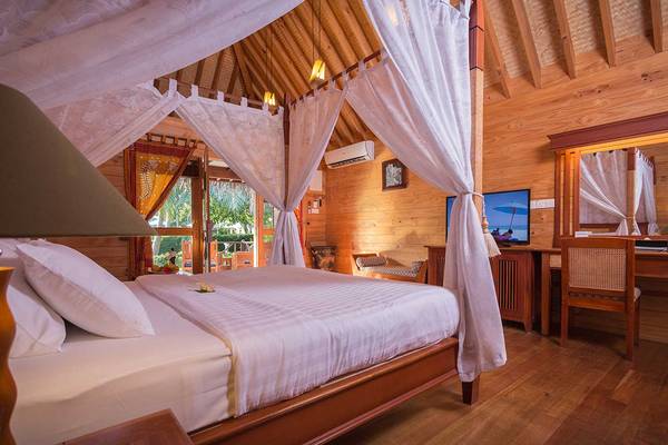 Innenansicht eines Schlafzimmers im Bandos Maldives Hotel mit einem Bett, Schreibtisch und Klimaanlage.