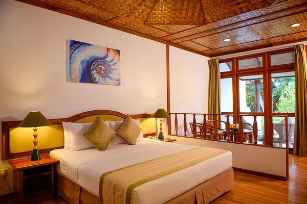 Innenansicht eines Zimmers im Bandos Maldives Hotel mit Bett, Lampen und Balkon.