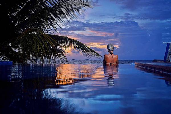 Einer Frau genießt den Blick auf das Meer im Pool des Bandos Maldives bei Sonnenuntergang.