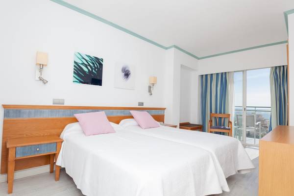 Zweibettzimmer im Timor Hotel mit Blick auf das Meer, weiße Bettwäsche und dekorativen Kunstwerken an der Wand.