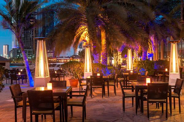 Außenbereich des Sheraton Abu Dhabi Hotel & Resort mit beleuchteten Palmen und Tischen.