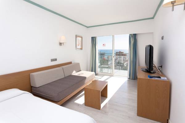 Innenansicht eines Zimmers im Timor Hotel mit Bett, Sofa und Balkon.