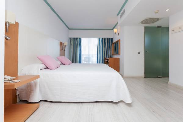 Innenansicht des Schlafzimmers im Timor Hotel mit weißem Bett, rosa Kissen, und hellem Boden.