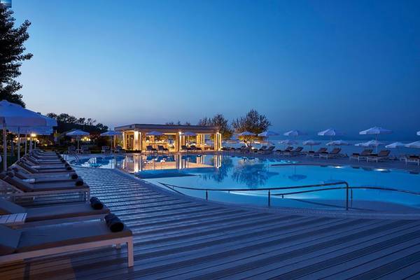 Abendlicher Blick auf den Pool des Capo Di Corfu Hotels mit Lounge-Sesseln und Sonnenschirmen.