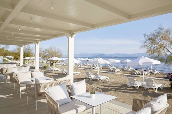 Außenterrasse des Capo Di Corfu Hotels mit weißen Sonnenliegen und Sonnenschirmen am Strand