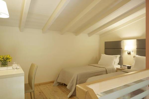 Doppelzimmer im Capo Di Corfu Hotel mit zwei Betten, Schreibtisch, Stuhl und Blumenvase.