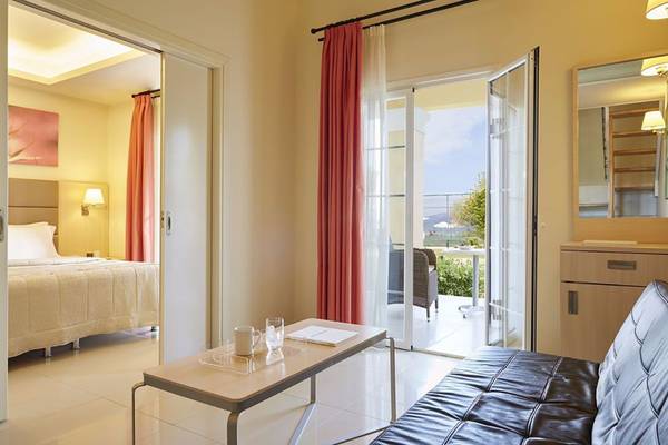 Innenansicht des Wohnbereichs im Capo Di Corfu Hotel mit offenem Balkon, Tisch und Sofa.