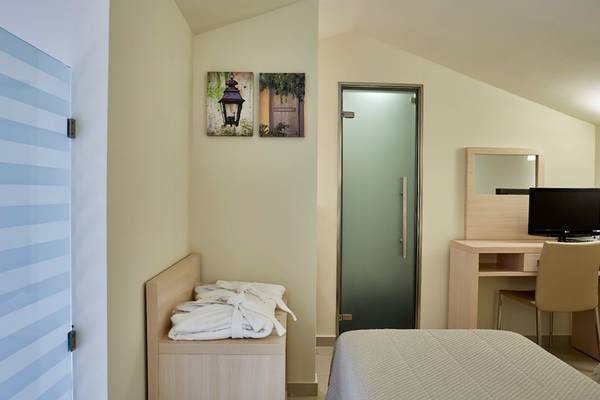 Ein modernes Hotelzimmer im Capo Di Corfu mit Bett, Nachttisch, Fernseher und Gemälden an der Wand.
