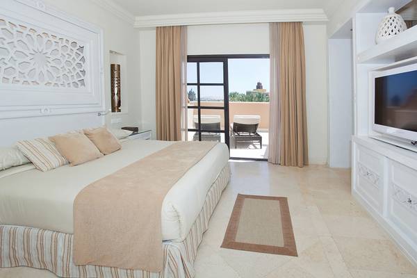 Schlafzimmer im Makadi Spa Hotel mit einem großen Bett, bequemen Kissen, und einer offenen Terrasse mit Blick auf einen Garten.
