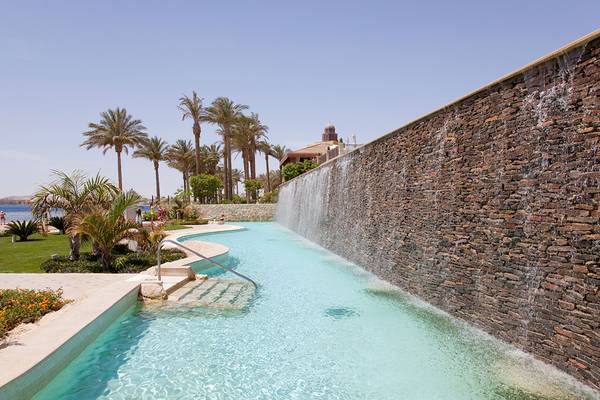 Poolbereich des Makadi Spa Hotels mit Wasserfall und Palmen im Hintergrund.