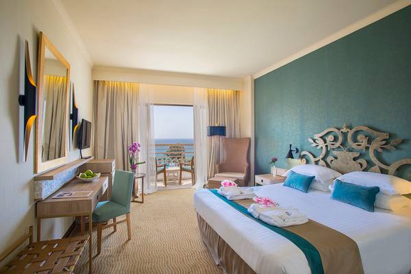 Hotelzimmer im GrandResort Limassol mit Meerblick, inklusive Bett, Schreibtisch, Stühle und Balkon.