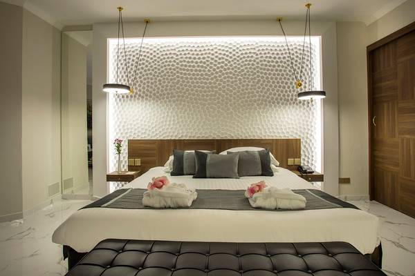 Schlafzimmer im GrandResort Limassol mit zeitgenössischem Design, einem Bett mit weißen und grauen Laken und zwei rosa Rosen auf der Decke.