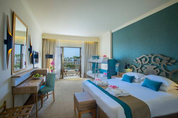 Innenansicht eines Hotelzimmers im GrandResort Limassol mit einem Doppelbett, einer Schlafcouch und einer Aussicht auf das Meer.