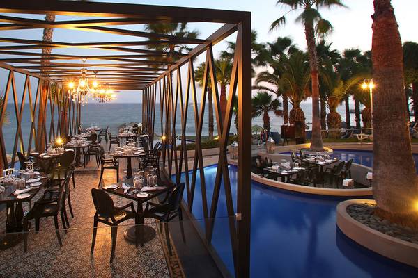 Außenbereich des GrandResort Limassol Restaurants mit blauem Pool und Blick auf das Meer.