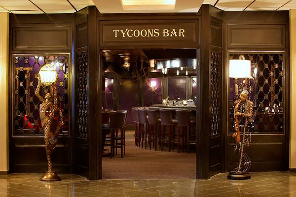 Eingang des Tycoons Bar im GrandResort Limassol mit zwei Statuen und einer offenen Tür.