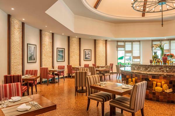 Innenansicht des Restaurants im Sheraton Abu Dhabi Hotel & Resort mit runden Tischen, Stühlen und einer Theke.