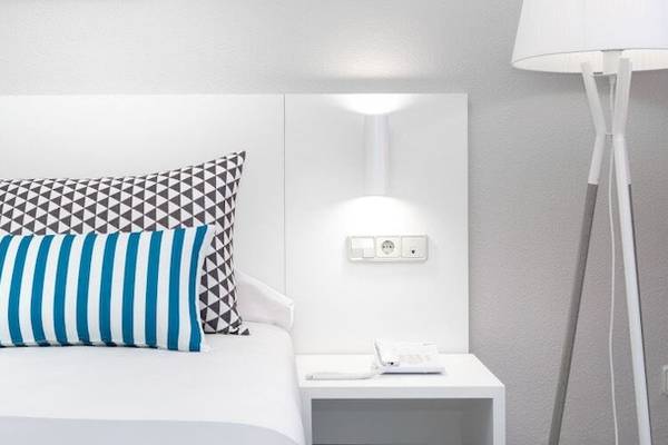 Ein modernes Hotelzimmer mit einem Bett, weißen Kopfteilen, drei Kissen, einer Lampe und einer Steckdose.