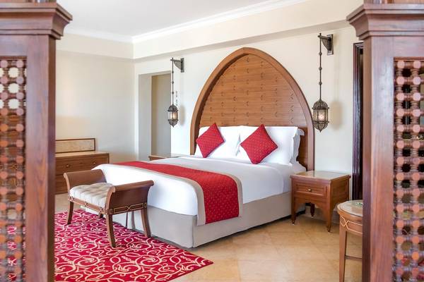 Innenansicht eines eleganten Hotelzimmers im Kempinski Hotel Soma Bay mit einem großen Bett, roten Kissen und zwei Nachttischen.