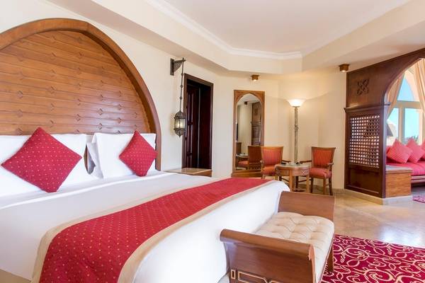 Luxuriöses Hotelzimmer im Kempinski Hotel Soma Bay mit rotem Bett, weißen Kissen und Holzmöbeln.