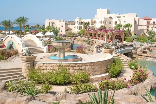 Außenansicht des Kempinski Hotels Soma Bay mit einem Brunnen, einer Brücke und tropischen Pflanzen.