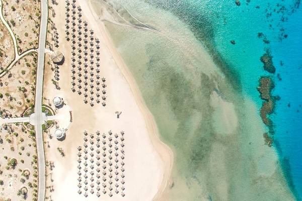 Luftaufnahme des Kempinski Hotels Soma Bay am Strand mit vielen Sonnenschirmen und blauem Wasser.