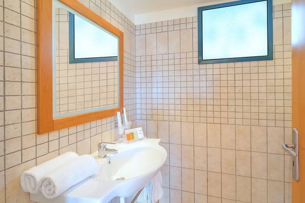 Badezimmer im Miramare Resort & Spa mit gefliesten Wänden, Spiegel, Waschbecken, Handtüchern und Fenstern.