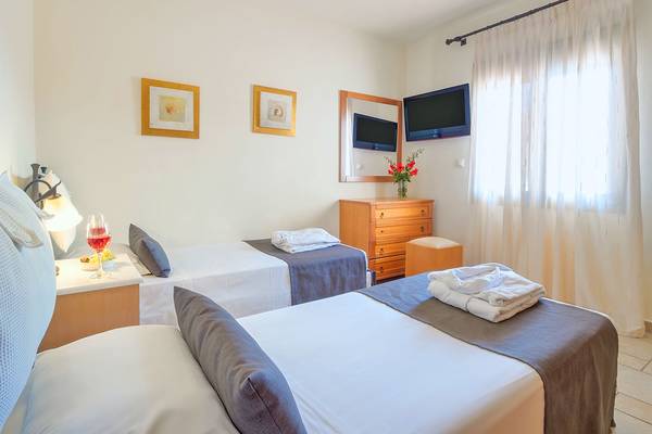 Zwei Betten in einem Hotelzimmer des Miramare Resort & Spa mit Fernseher, Nachttischen und einem Fenster mit Vorhängen.