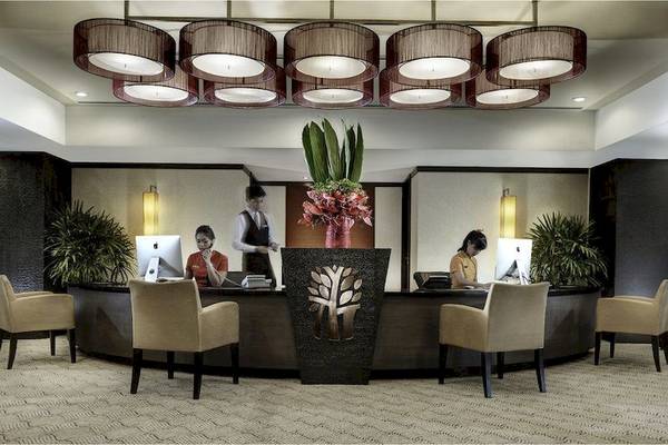 Empfang des Banyan Tree Bangkok Hotels mit drei Angestellten an Schreibtischen und einem großen Blumenarrangement.