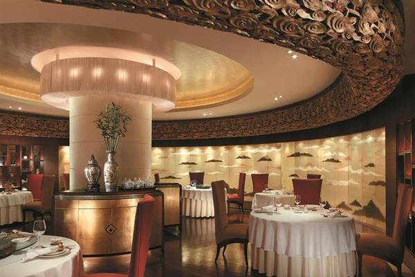 Innenansicht des Restaurants im Shangri-La Hotel in Dubai mit runden Tischen, roten Stühlen und einer zentralen Säule.