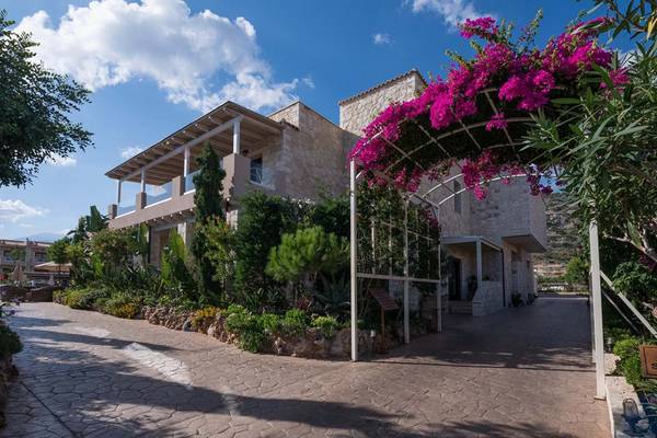 Außenansicht des Cactus Royal Hotels mit Steinmauer, rosa Blumen und gepflastertem Weg.
