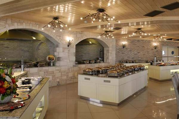 Innenbereich des Cactus Royal Hotels mit vielen Tischen und Stühlen, Buffets und dekorativen Kronleuchtern.