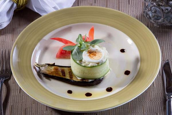 Gegrillte Aubergine mit Gurkenstreifen und Ei auf einem weißen Teller serviert.