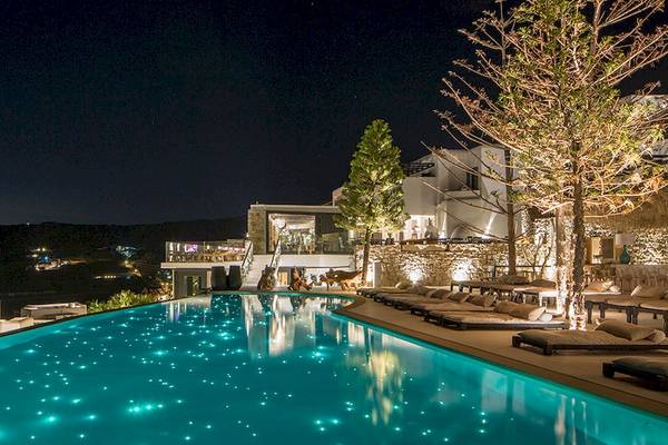 Nachtansicht des Pools im Myconian Utopia Resort mit beleuchteten Bäumen und Loungeliegen.