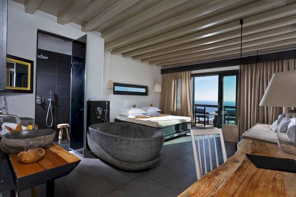 Innenansicht eines Zimmers im Myconian Utopia Resort mit Badewanne, Bett, Tisch und Aussicht auf das Meer.