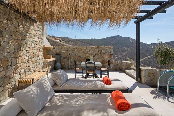 Terrasse des Myconian Utopia Resorts mit Loungebetten, Tisch und Blick auf Berge