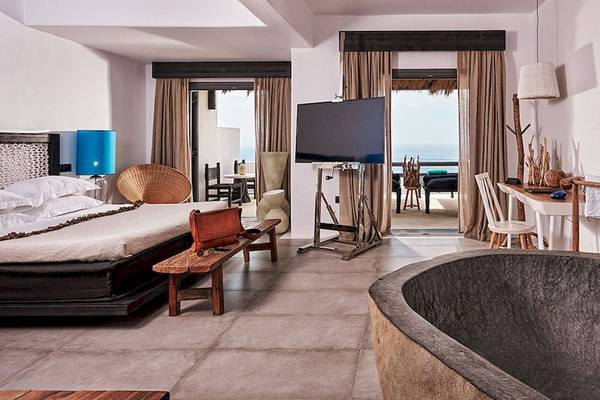 Ein modernes Hotelzimmer mit einem großen Bett, Fernseher, Schreibtisch und Badewanne mit Meerblick.