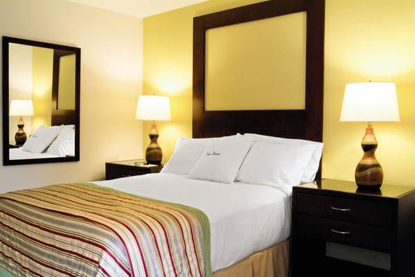 Doppelbett im Hotelzimmer im Fiesta Resort All Inclusive mit gelben Wänden, Bettwäsche und zwei Nachttischen.