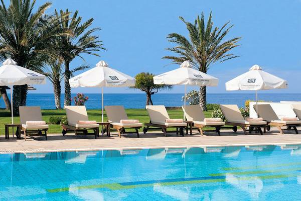 Reihe von Sonnenliegen und Sonnenschirmen am Pool des Athena Royal Beach Hotel mit Blick auf das Meer.