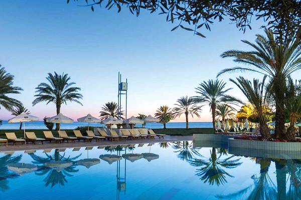 Poolbereich des Athena Royal Beach Hotel bei Abendstimmung mit Palmen und Sonnenliegen