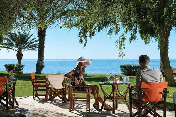 Zwei Personen sitzen auf Stühlen mit Blick auf das Meer im Athena Royal Beach Hotel.